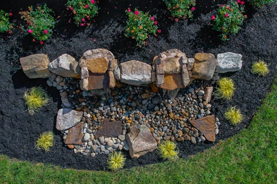 Genesis D - A rock garden with a water feature surrounded by flowers and grass