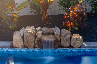 Genesis M -  - A stack of rocks next to a blue swimming pool with water splashing out of it