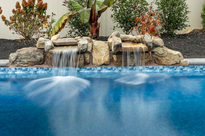 Genesis M -  - A swimming pool with a waterfall feature surrounded by plants and shrubs