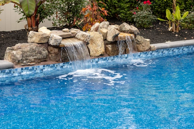 Genesis M -  - A swimming pool with a waterfall in the middle surrounded by plants and flowers