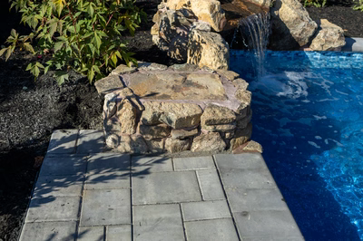 Genesis P - A stone fountain in the middle of a swimming pool surrounded by lush greenery