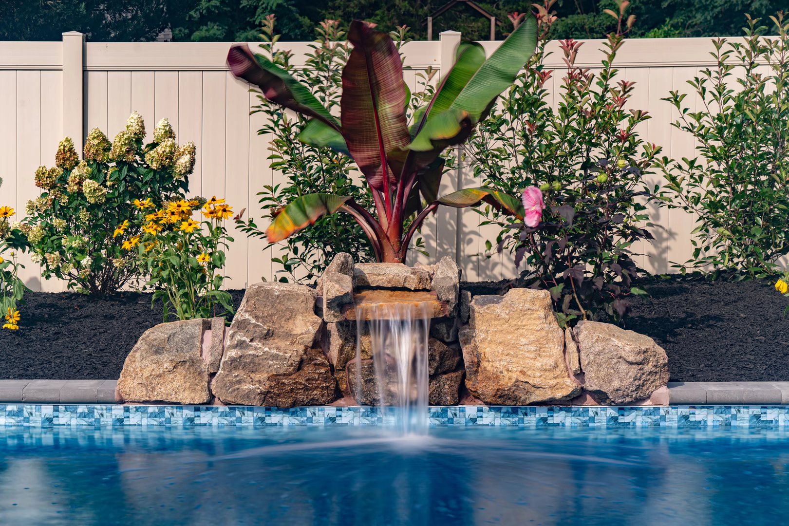 Natural stone boulder waterfall cascading into a pool with lush tropical garden plants
