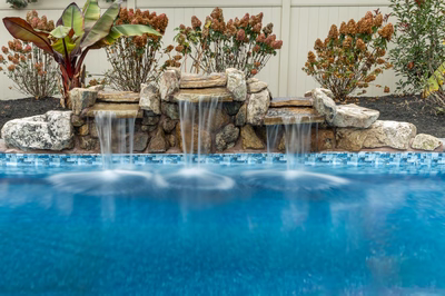 Genesis T -  - A swimming pool with a waterfall feature surrounded by plants and flowers