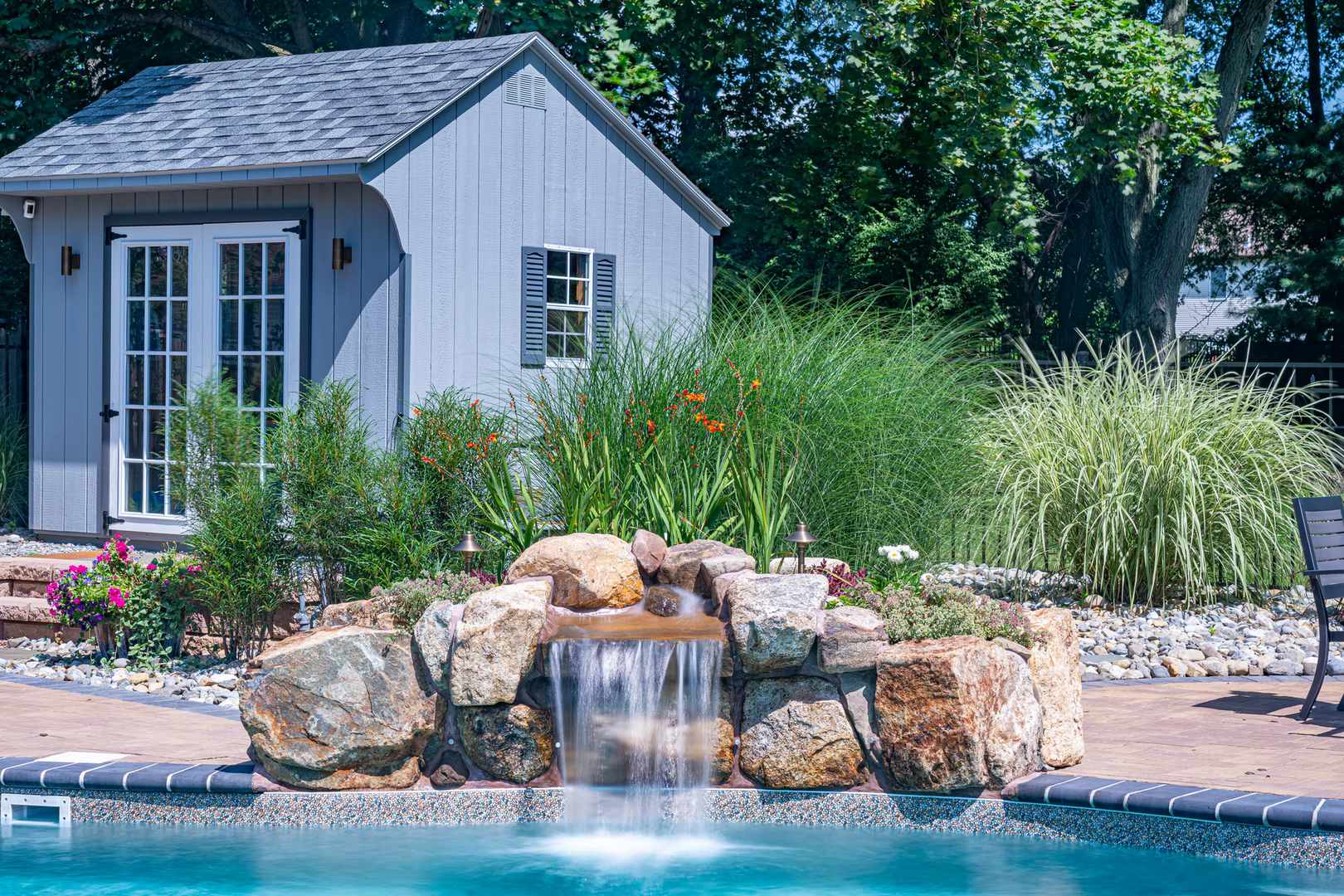 Single-tier natural stone boulder waterfall cascading into a pool beside lush ornamental garden plants