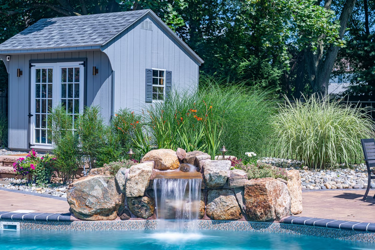 Natural stone boulder waterfall cascading into a pool beside lush ornamental garden plants