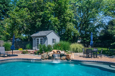 Georgiana C - Hillsborough, NJ - A backyard with a pool and a small shed surrounded by lush greenery