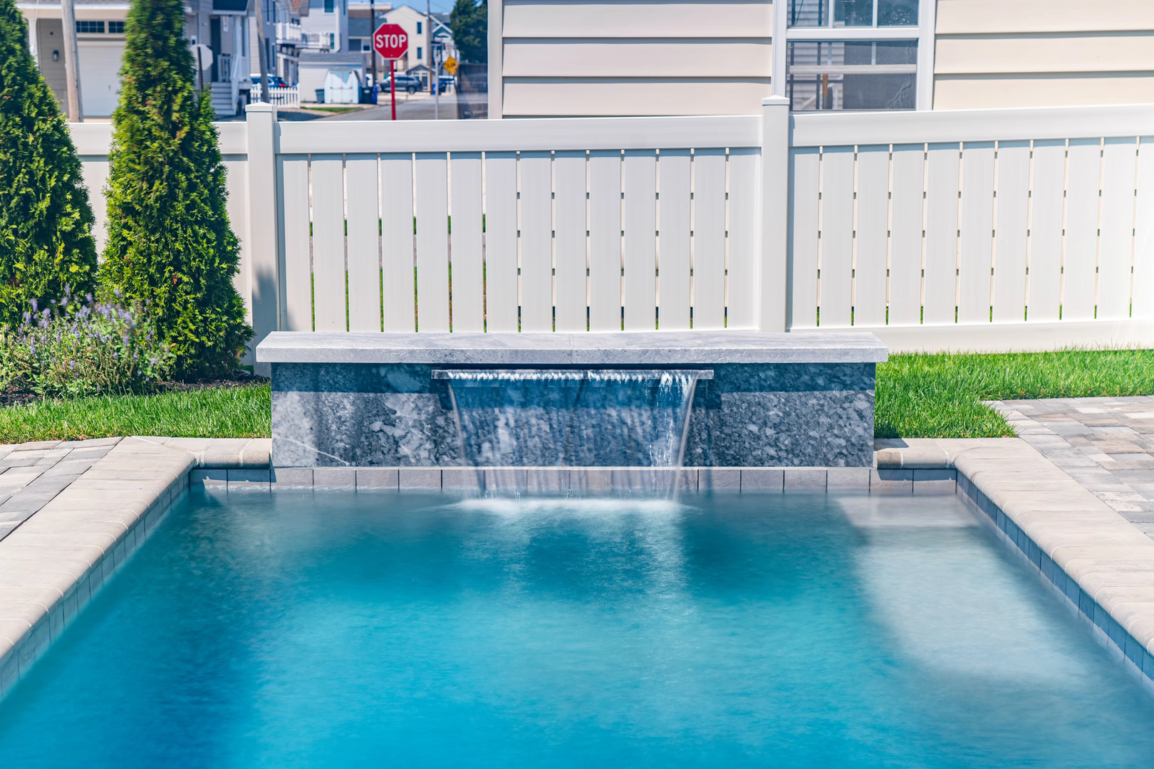 Single-tier natural stone sheer descent waterfall cascading into pool with surrounding green landscaping