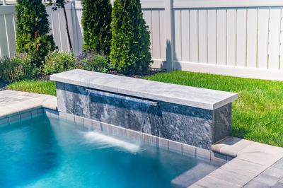 Gibbs D - Avalon, NJ - A concrete bench with a waterfall in the middle of a swimming pool surrounded by lush green grass and a white fence