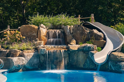 Gikira B - Bethlehem, PA - A swimming pool with a waterfall and a slide surrounded by lush greenery
