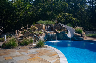 Gikira C - Bethlehem, PA - A swimming pool with a waterfall and a slide surrounded by lush greenery