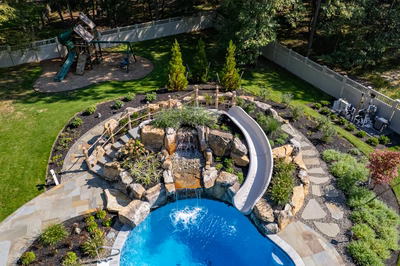 Gikira K - Bethlehem, PA - A backyard with a swimming pool and a water feature, surrounded by lush green grass and trees