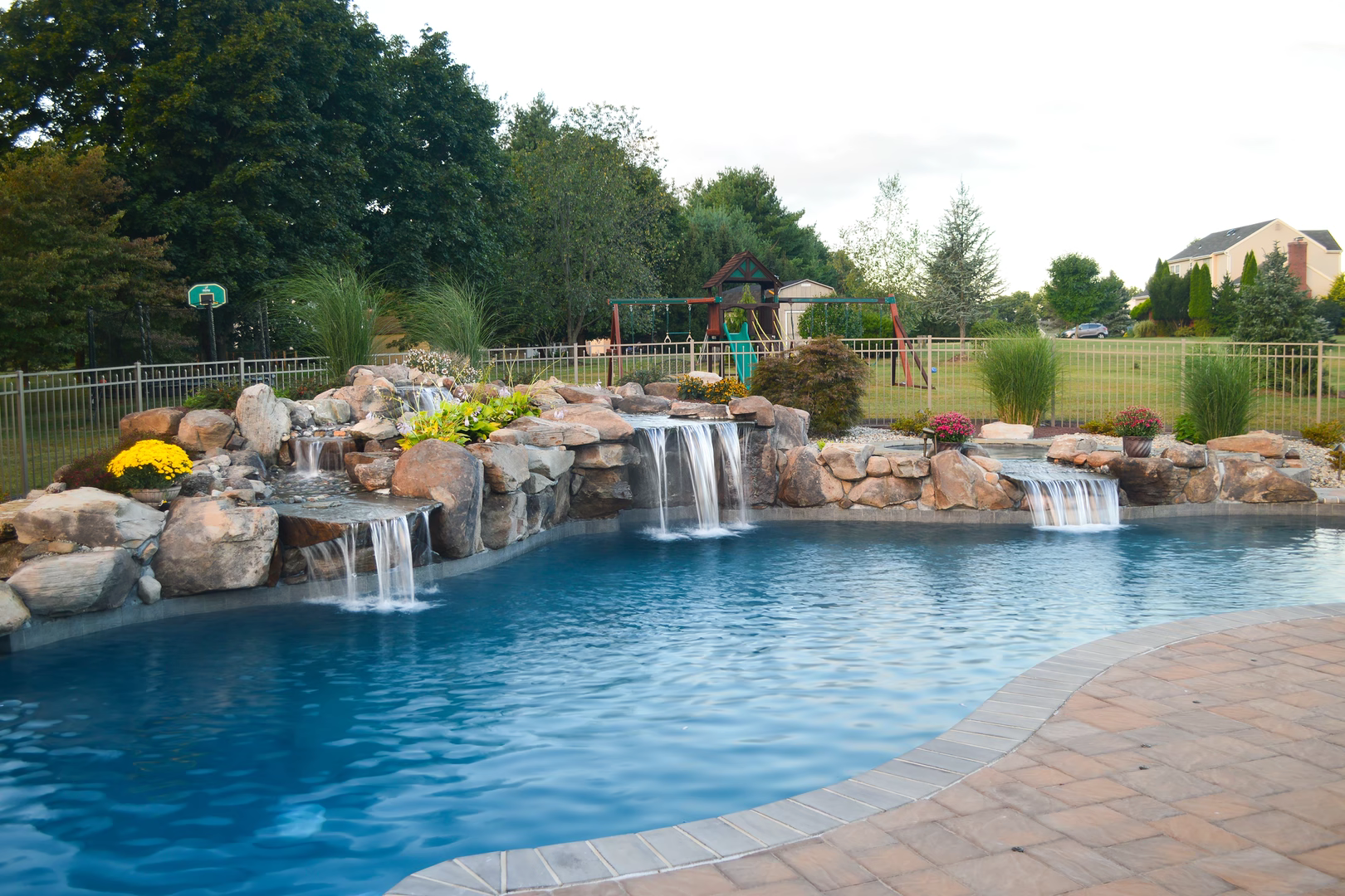 Cascading multi-tiered stone boulder waterfalls flowing into a swimming pool with vibrant garden plants