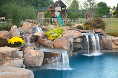 Ginga D - Ringoes, NJ - A backyard pool with a waterfall feature and a play structure in the background