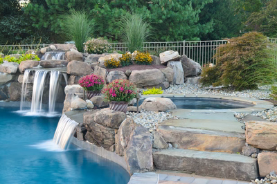 Ginga E - Ringoes, NJ - A swimming pool with a waterfall surrounded by rocks and flowers.