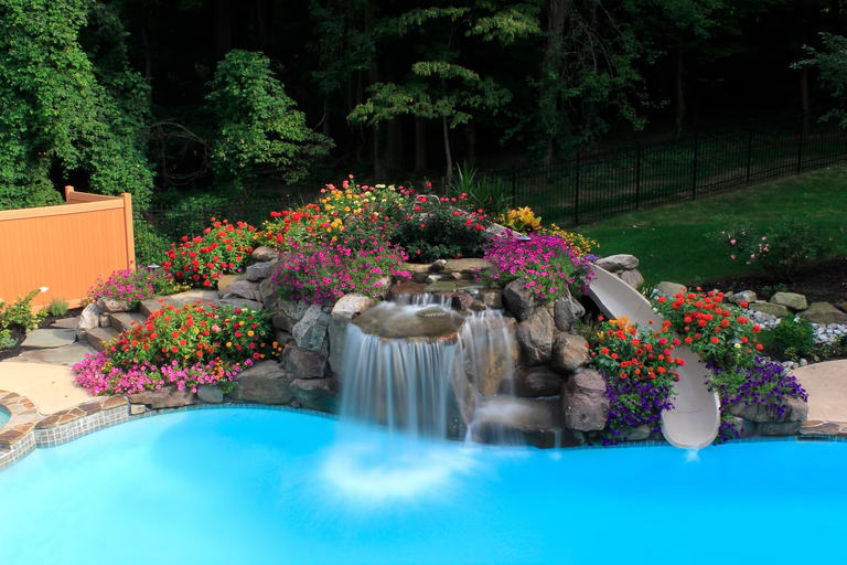 Natural stone boulder waterfall cascading into a pool surrounded by lush, colorful flowers