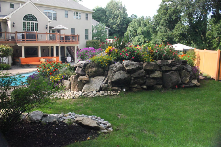 Natural stone boulder waterfall cascading into a pool surrounded by lush garden flowers