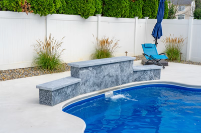Haifoss C - Sicklerville, NJ - A blue swimming pool with a waterfall feature and a bench in a backyard setting