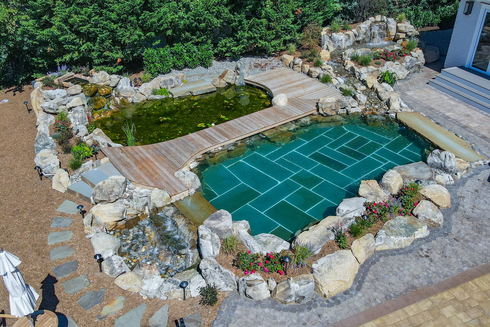 Natural stone waterfalls cascading into a tiled pool surrounded by lush green plants