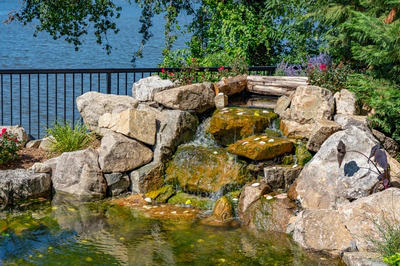 Havasu F - Manasquan, NJ - A small waterfall cascades over rocks into a serene pond surrounded by lush greenery and flowers