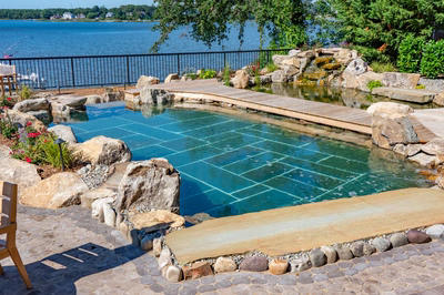 Havasu U - Manasquan, NJ - A large rectangular swimming pool surrounded by rocks and plants, with a wooden walkway leading to it
