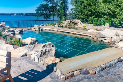 Havasu W - Manasquan, NJ - A large rectangular swimming pool surrounded by rocks and greenery, with a wooden walkway leading to it