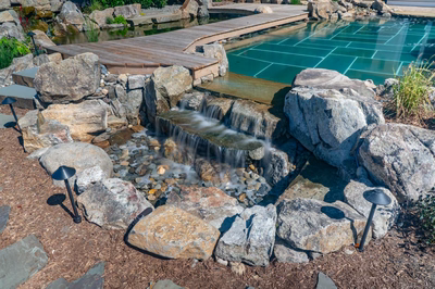 Havasu Z - Manasquan, NJ - A wooden bridge over a small waterfall surrounded by rocks and plants near a swimming pool