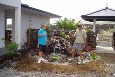 Hawaii5024J - A large rock waterfall in the middle of a swimming pool surrounded by lush greenery
