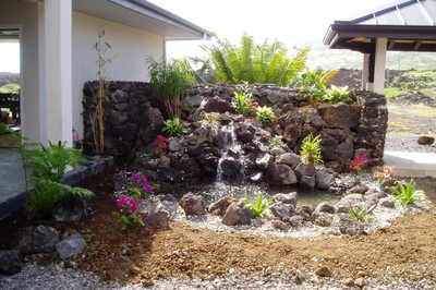 Hawaii5024K - A large rock waterfall in the middle of a swimming pool surrounded by lush greenery