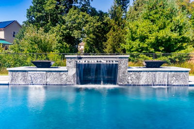 Haymeadow C - Mullica Hill, NJ - A swimming pool with a waterfall feature in the middle surrounded by trees and a house in the background