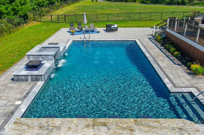Haymeadow L - Mullica Hill, NJ - A rectangular swimming pool surrounded by lush green grass and a stone patio with a waterfall feature