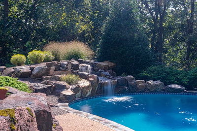 Hemlock H - East Petersburg, PA - A swimming pool surrounded by lush greenery and rocks with a waterfall