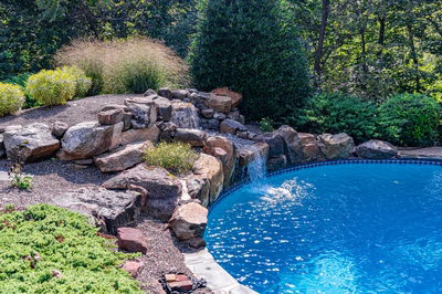 Hemlock J - East Petersburg, PA - A swimming pool surrounded by lush greenery and rocks with a waterfall