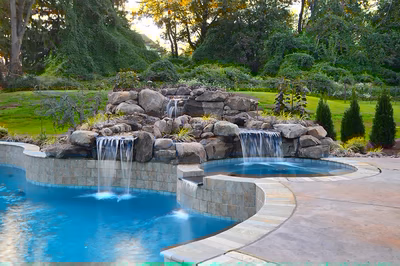 Himmilstein-D - A swimming pool lit up at night with a waterfall and rocks in the background