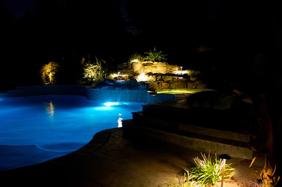 Himmilstein-I - A swimming pool lit up at night with a waterfall and rocks in the background