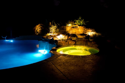 Himmilstein-J - A swimming pool lit up at night with a waterfall and rocks in the background