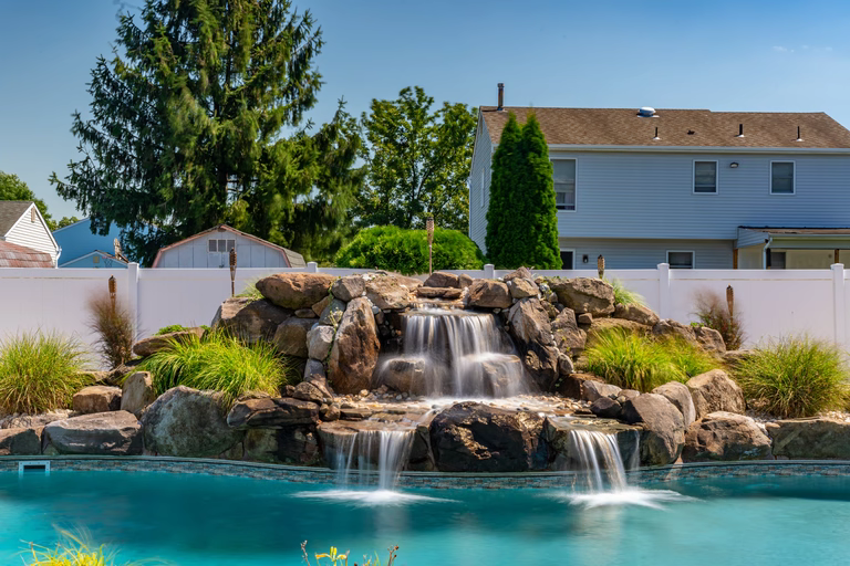 Natural stone boulder waterfall cascading into a pool with surrounding ornamental grasses