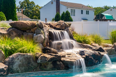 Hinemoa C - Turnersville, NJ - A large rock waterfall in a backyard with a white fence and a house in the background