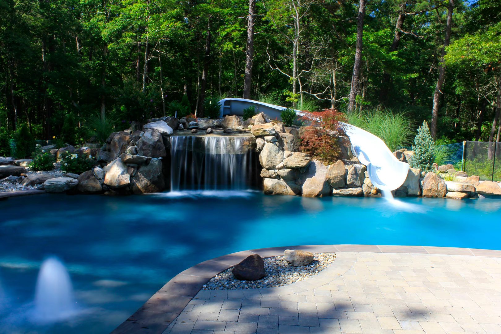 Natural stone boulder waterfall cascading into a pool surrounded by lush forest greenery