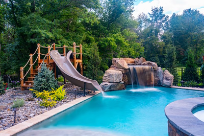 Horsetail B - Marlton, NJ - A swimming pool with a waterfall and a play structure surrounded by lush greenery
