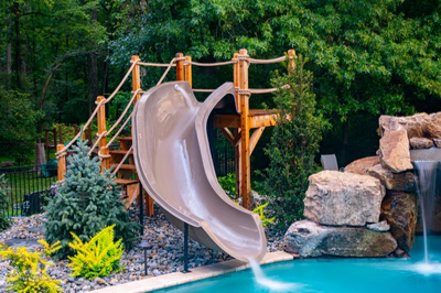 Horsetail D - Marlton, NJ - A wooden play structure with a water slide next to a swimming pool surrounded by lush greenery