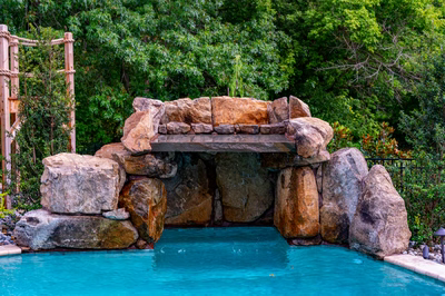Horsetail G - Marlton, NJ - A large rock structure in the middle of a swimming pool surrounded by lush greenery