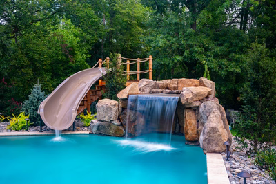 Horsetail H - Marlton, NJ - A swimming pool with a water feature and a slide surrounded by lush greenery