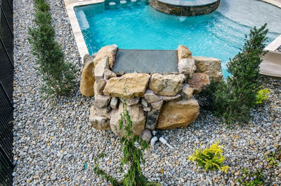 Horsetail N - Marlton, NJ - A backyard with a swimming pool and a water feature surrounded by rocks and plants