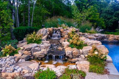 Howick E - Ivyland, PA - A rock garden with a waterfall and a swimming pool surrounded by lush greenery