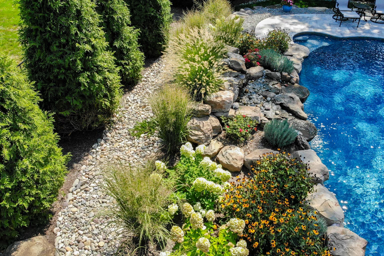 Boulder waterfall cascading into a pool surrounded by lush grasses and flowers