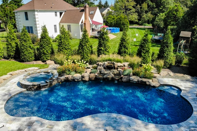 Huka H - Moorestown, NJ - A large backyard with a swimming pool surrounded by lush greenery and landscaping