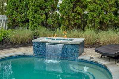 Single-tier blue tiled fire feature cascading sheer water into pool surrounded by lush garden greenery
