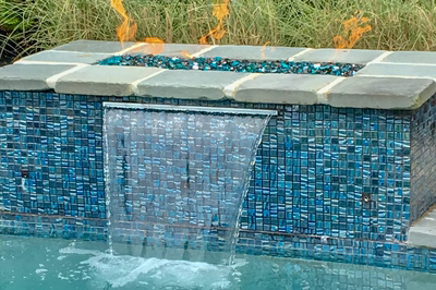 Single-tier sheer descent waterfall cascading from a tiled fire pit into a pool with greenery