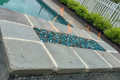 Natural stone boulder waterfall with multiple tiers cascading into a pool beside green bushes