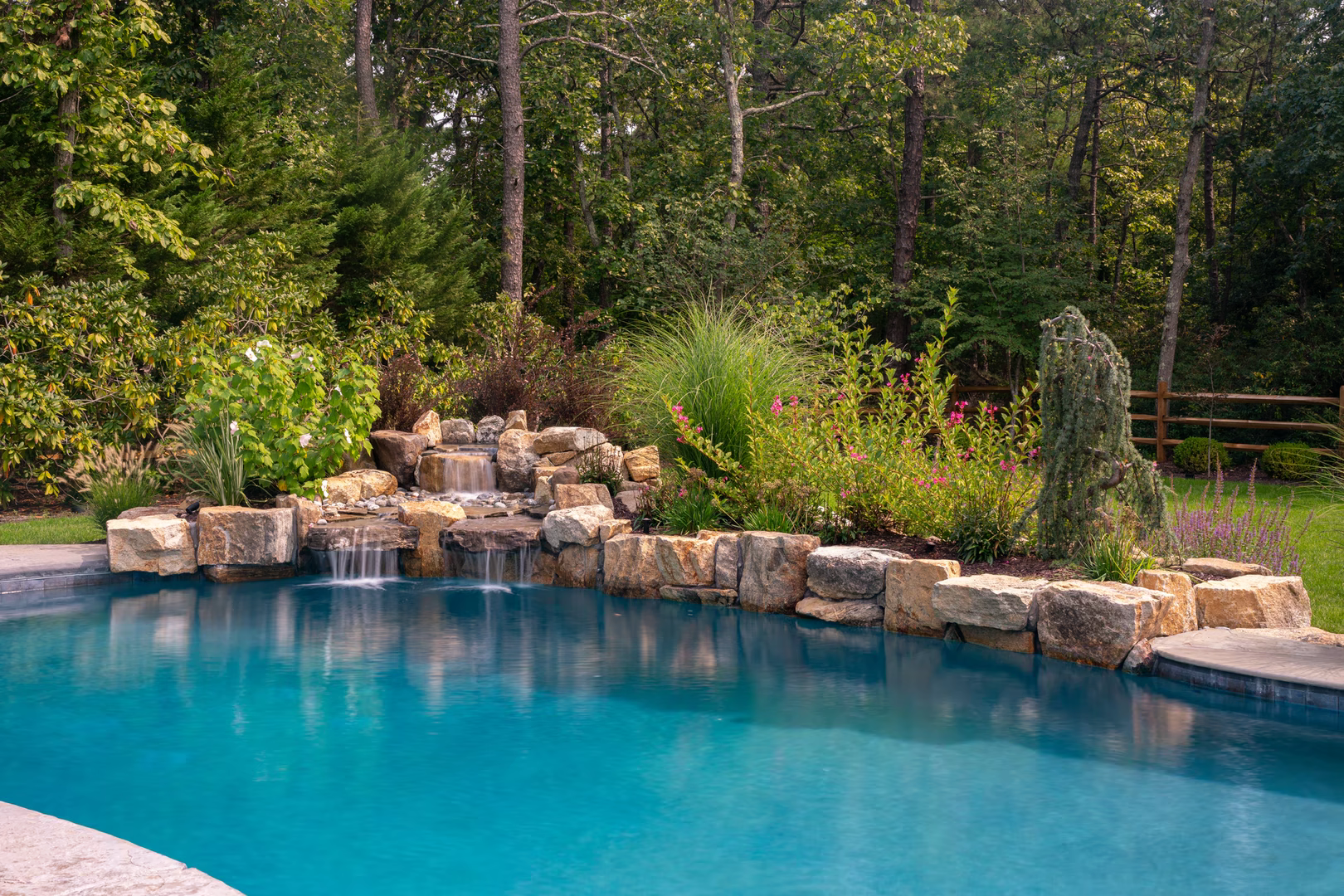 Natural stone boulder waterfall cascading into a pool surrounded by lush garden greenery